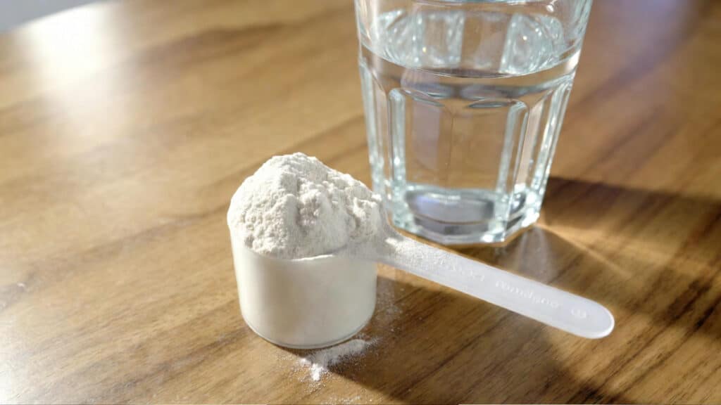 Measuring scoop of creatine monohydrate powder next to a glass of water on a wooden surface
